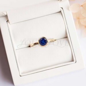 Bezel-set round sapphire ring in yellow gold displayed in a cushioned holder.