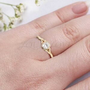 Oval moissanite bezel-set ring with twisted branch band and leaf-accented side stones.