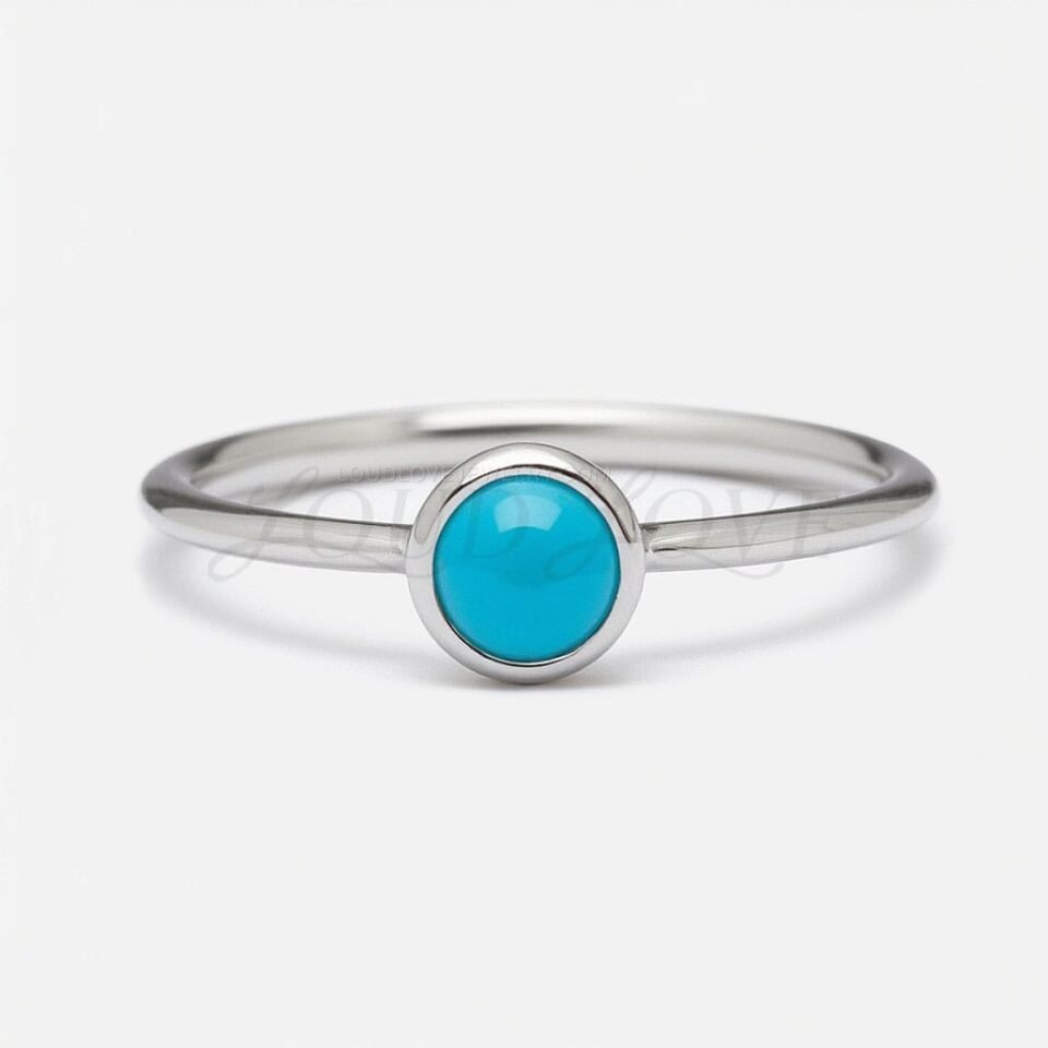Front angle of solitaire ring with turquoise cabochon set in a smooth silver bezel mount.