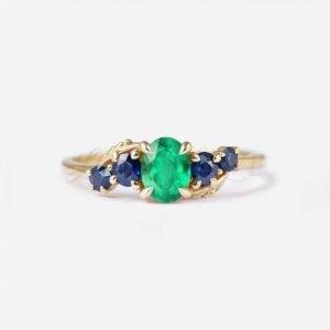 Oval lab-grown emerald with two side sapphires set in an organic gold branch band.
