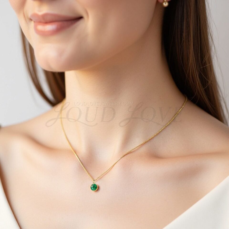 Minimalist necklace with bezel-set emerald, styled to honor May birthdays with natural elegance.