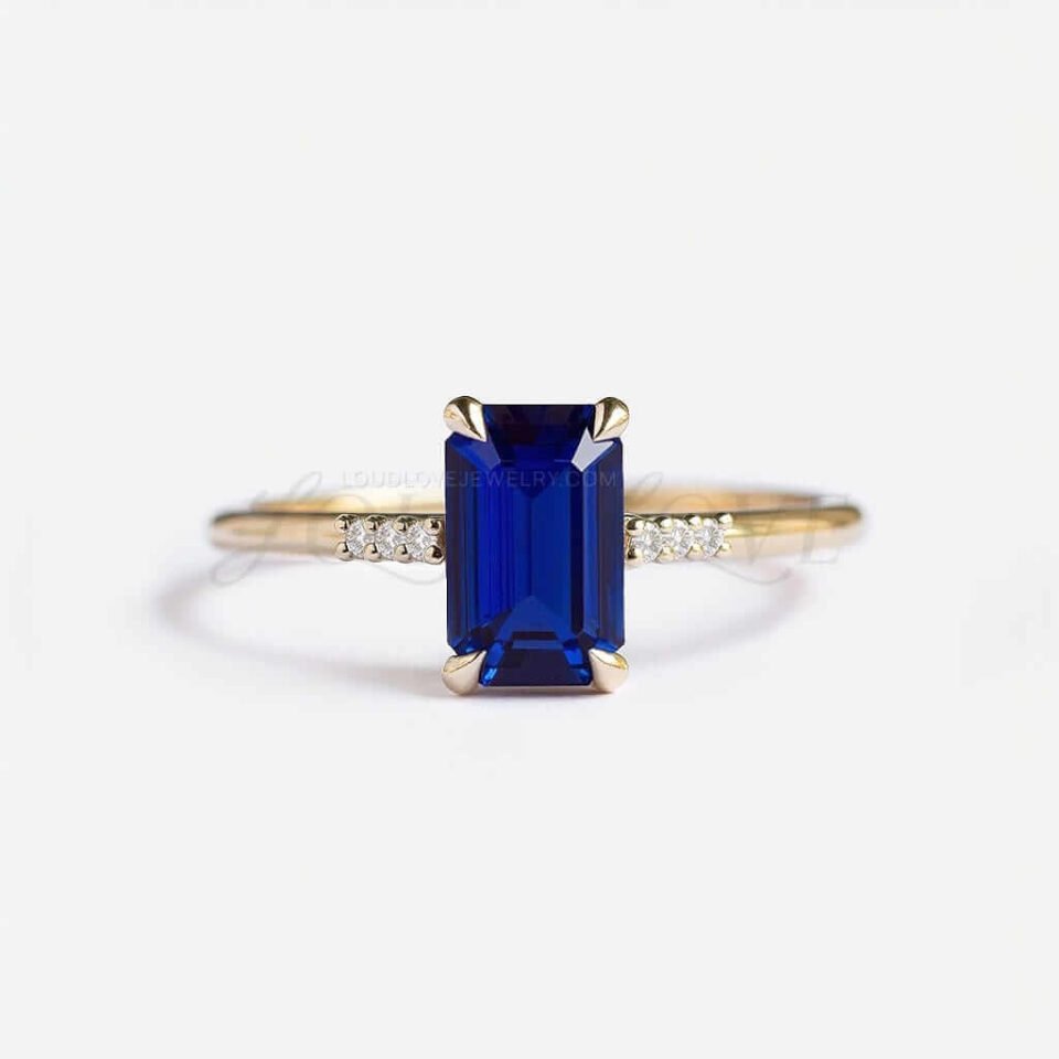 Emerald cut lab sapphire in yellow gold with six side stones in a modern setting.