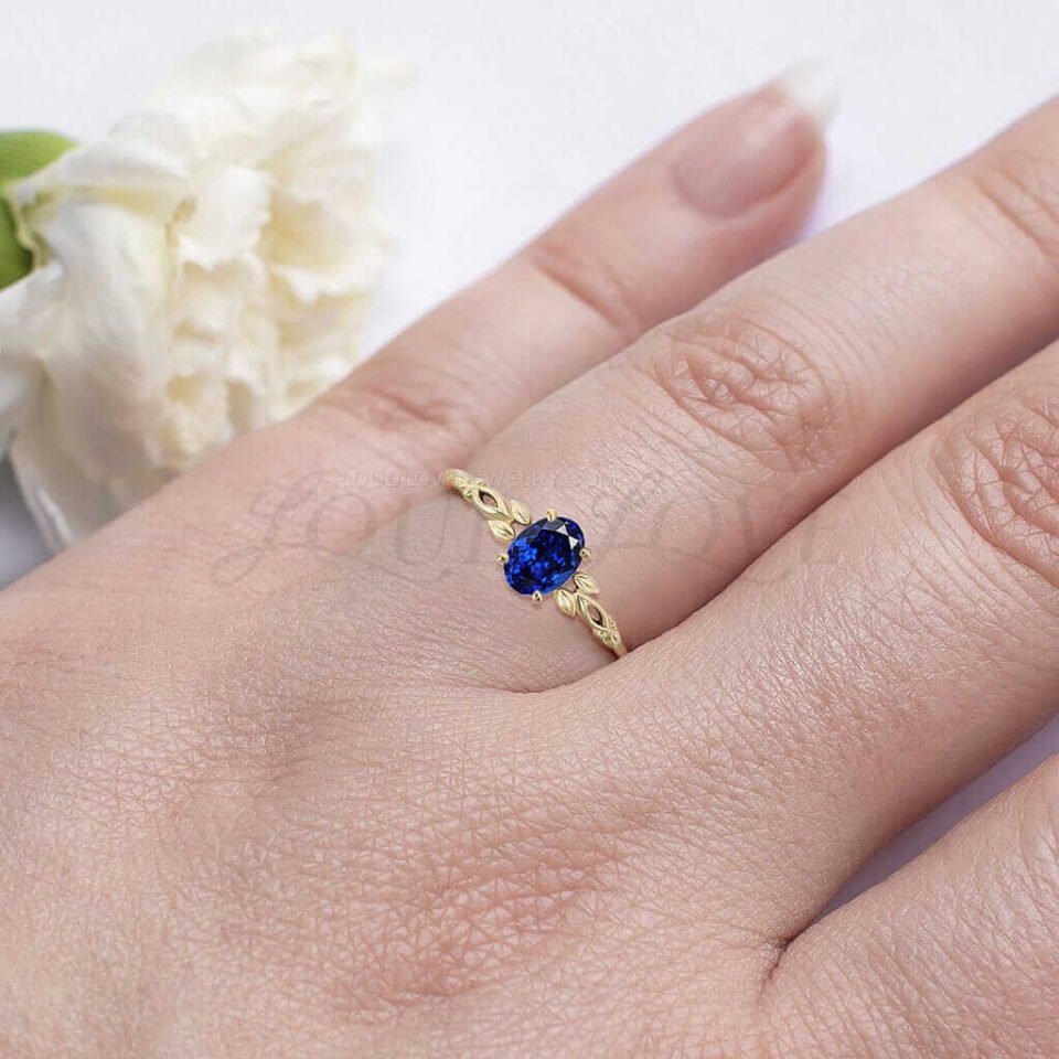 Gold ring with oval sapphire and botanical leaf accents worn as a unique engagement ring.