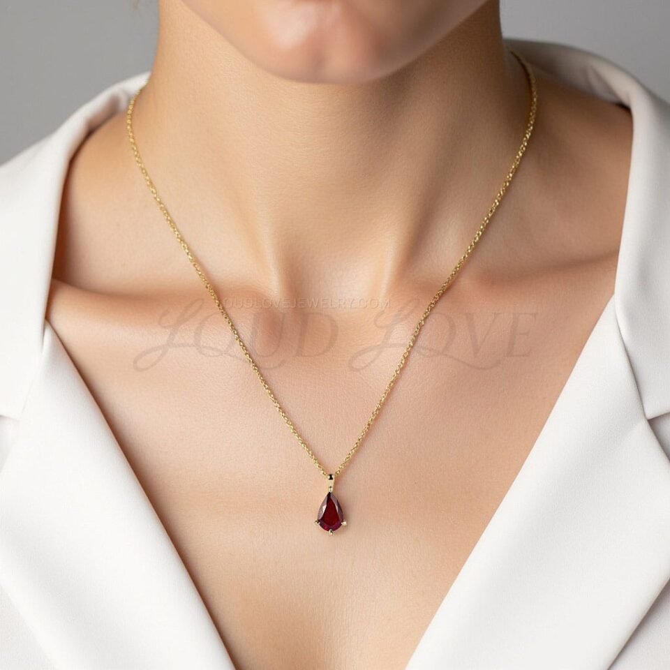 Gold necklace with deep red garnet in a pear shape, worn to celebrate January birthdays.