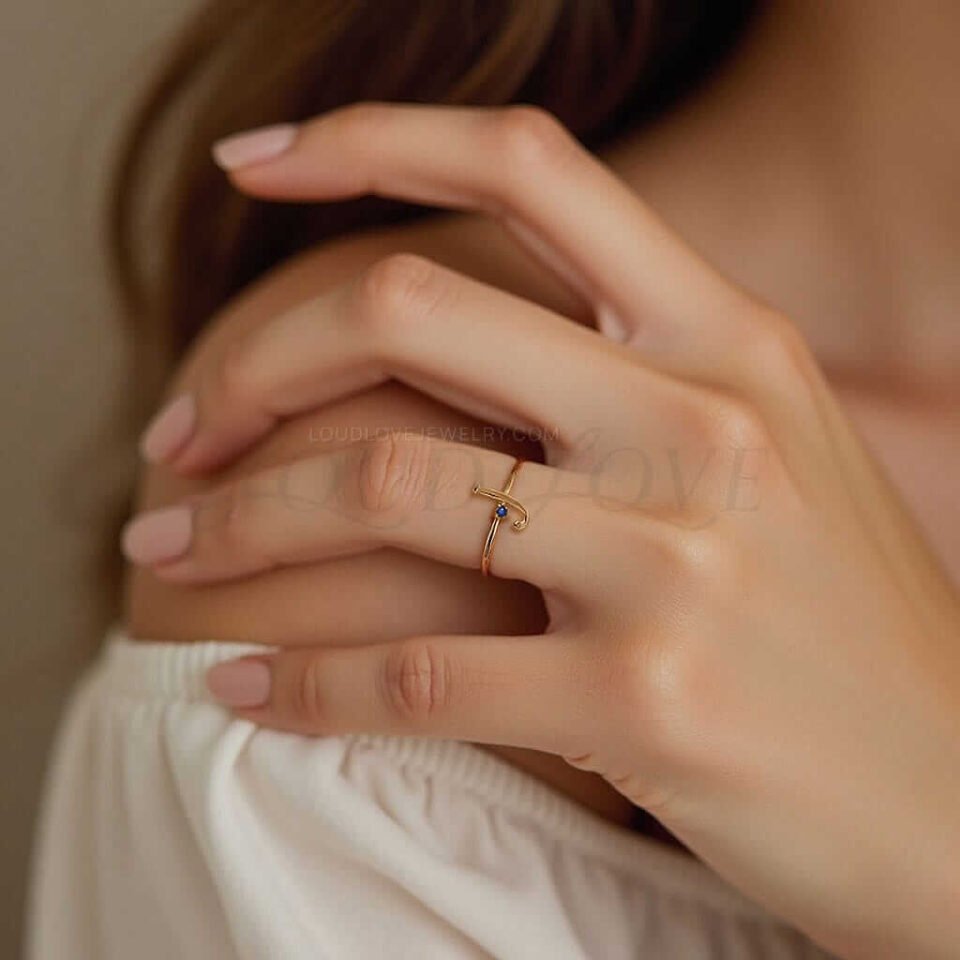 A person wearing a gold ring with the initial "J" and a blue birthstone on their finger.
