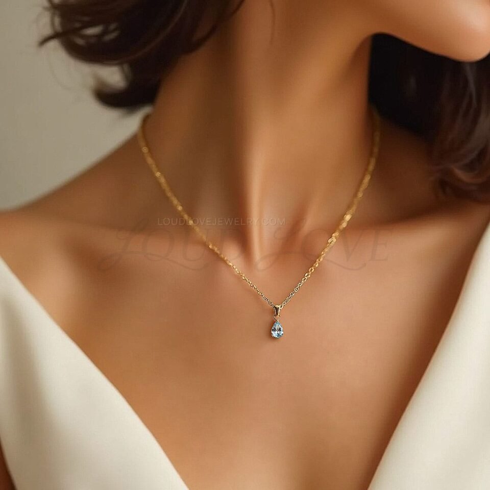 Teardrop-shaped aquamarine pendant in gold, shown worn on a model's neck.