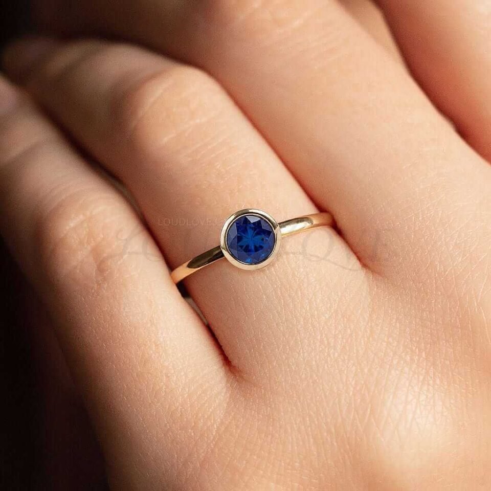 Yellow gold solitaire ring with round bezel-set sapphire worn as a classic engagement ring.