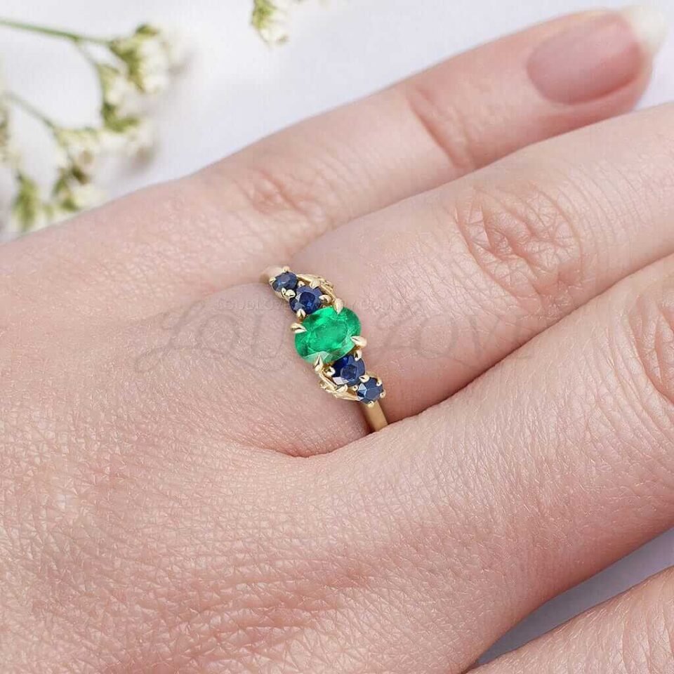 Nature-inspired gold ring with oval emerald and blue sapphire side stones worn on hand.
