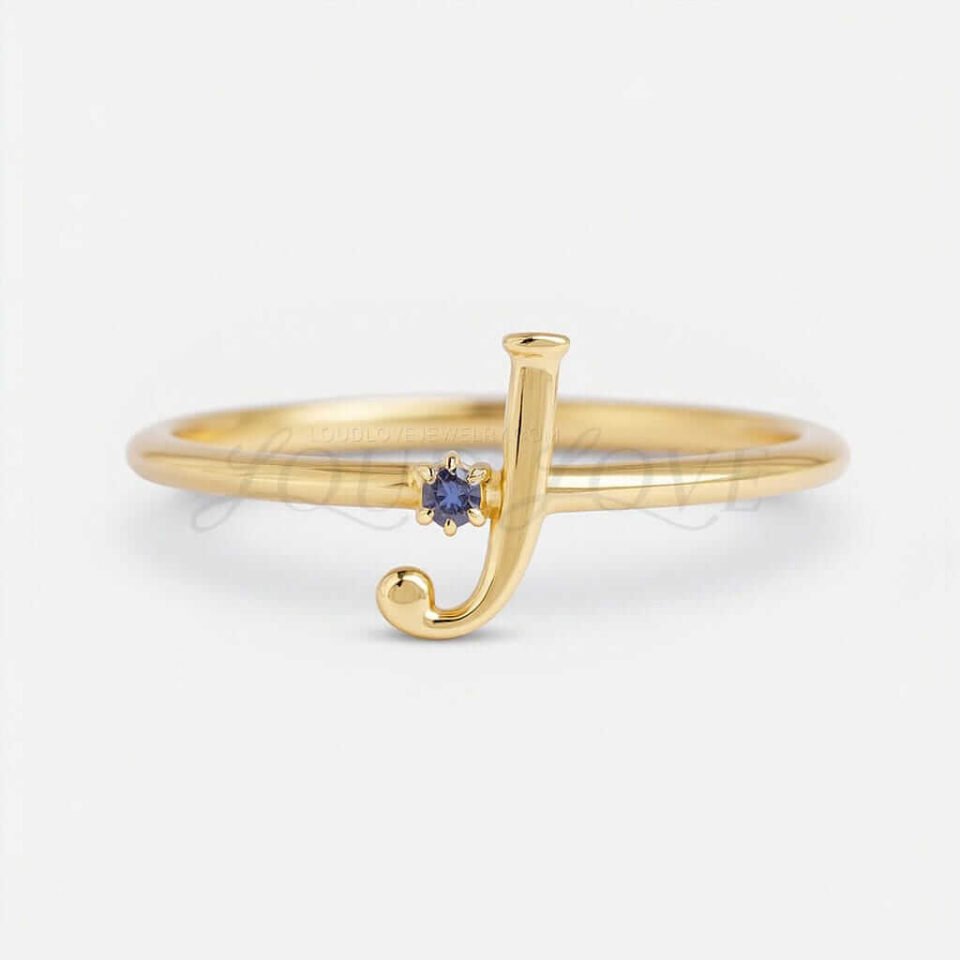A gold ring featuring the initial "J" and a blue colored gemstone on a white background.