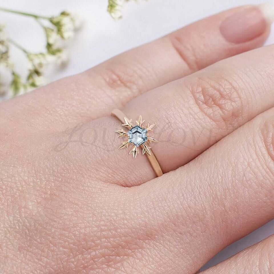 Delicate rose gold ring with aquamarine snowflake design worn as a promise or engagement ring.