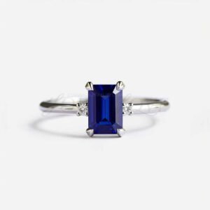 Emerald cut lab sapphire with two side stones on a sleek platinum band.