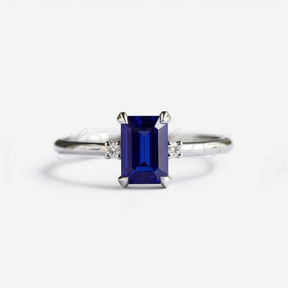 Emerald cut lab sapphire with two side stones on a sleek platinum band.