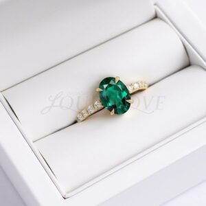 Oval lab emerald and moissanite ring displayed in a soft ring cushion.
