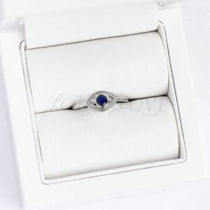 Round sapphire evil eye ring displayed in a soft cushioned jewelry holder.