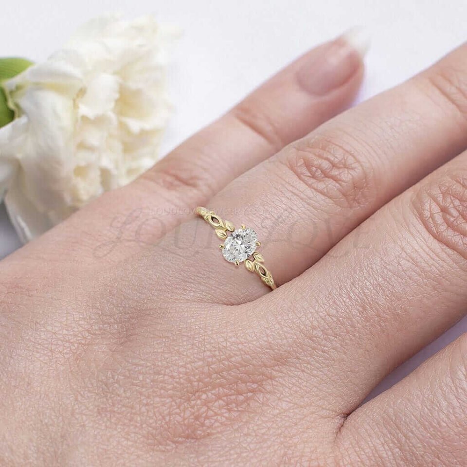 Nature-inspired engagement ring with oval moissanite and yellow gold leaf band worn on hand.