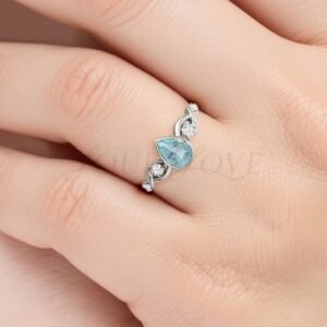White gold ring with pear bezel aquamarine and ocean-inspired side detailing worn on hand.
