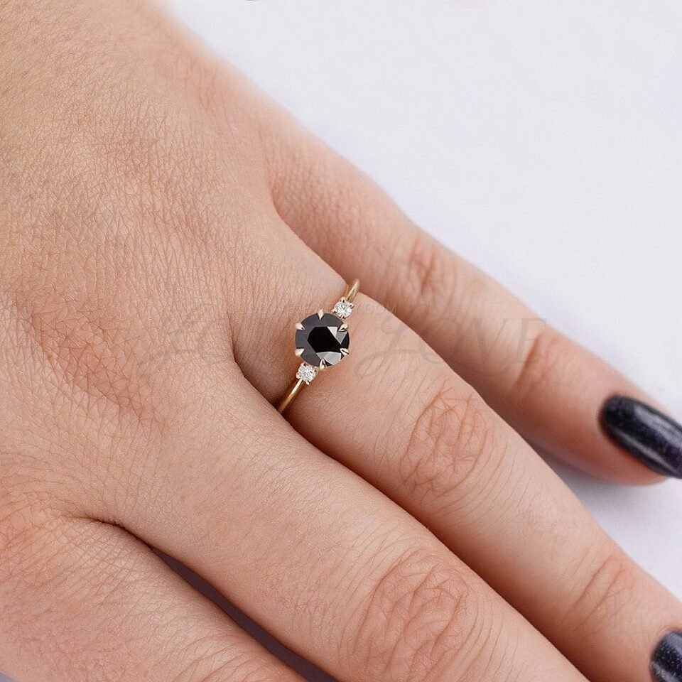 Three-stone ring with black center diamond and side stones in gold, worn on hand.