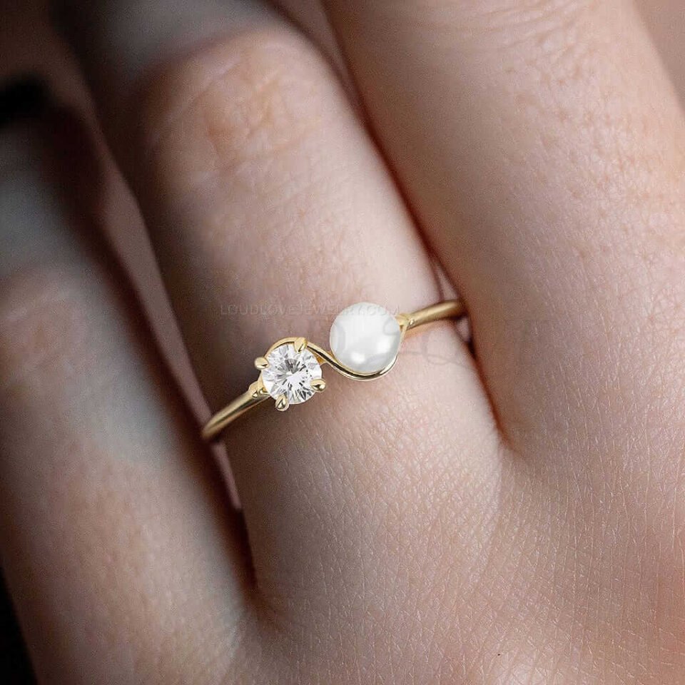Thin gold band with pearl and diamond stones worn as a unique two-stone engagement ring.