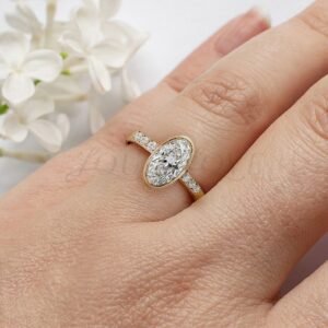 Moissanite engagement ring with bezel setting and six side stones shown on hand.