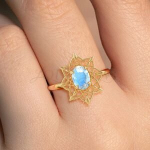Yellow gold ring with oval moonstone and intricate dreamcatcher motif worn on hand.