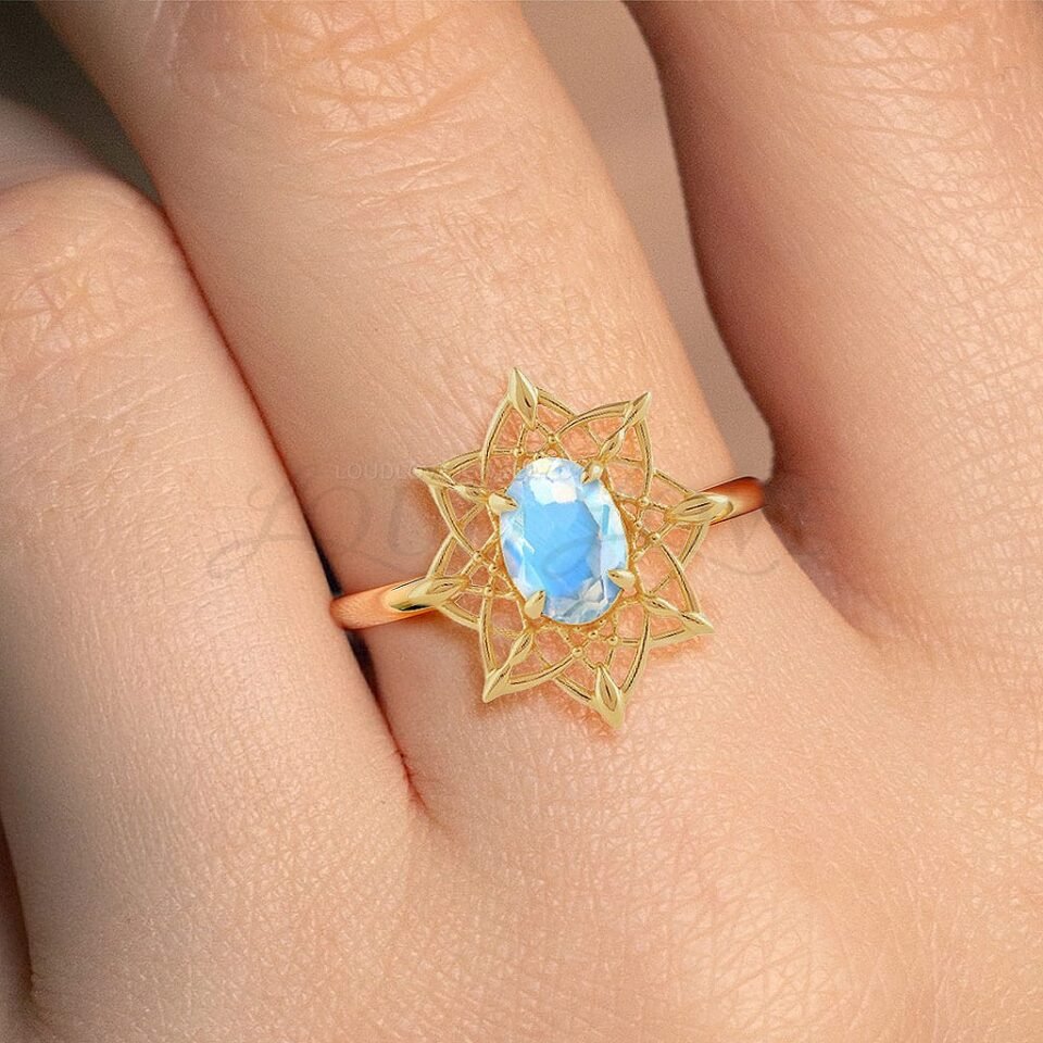 Yellow gold ring with oval moonstone and intricate dreamcatcher motif worn on hand.