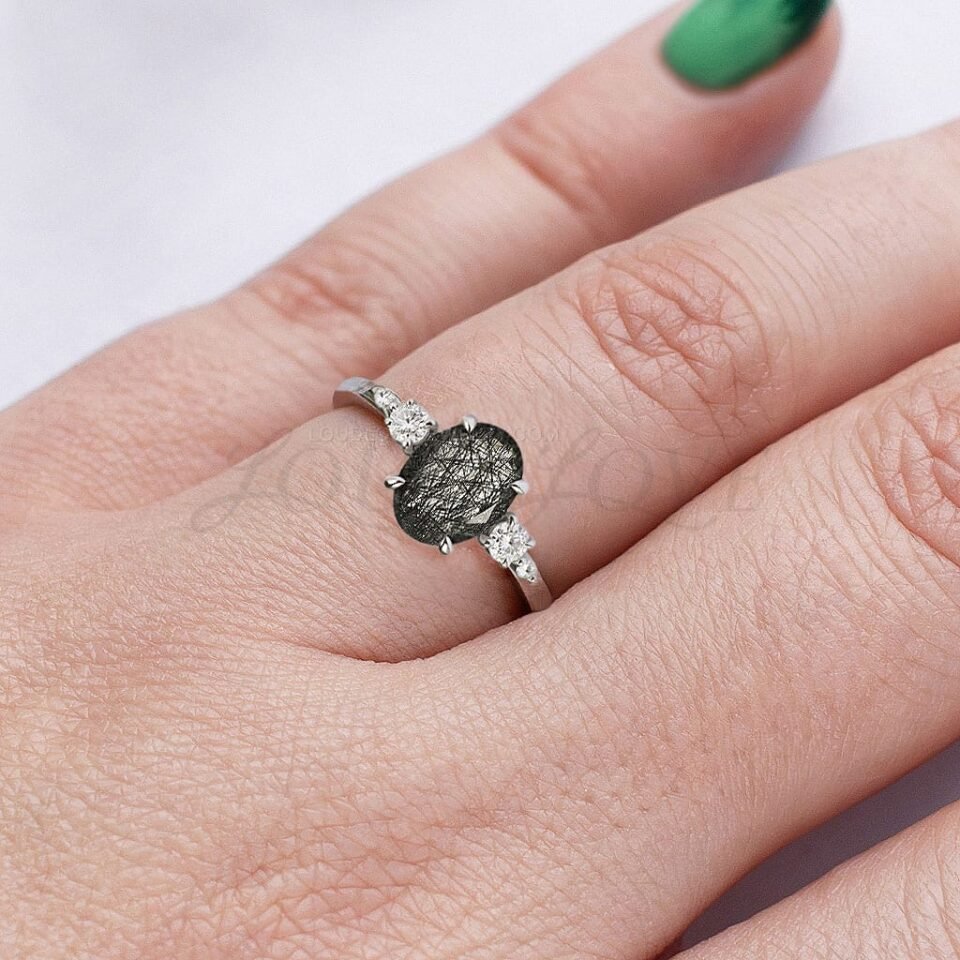 Black rutilated quartz ring with oval stone and round side stones, worn on hand for display.