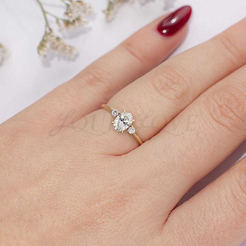 Elegant three-stone oval engagement ring with round side stones, shown on hand.
