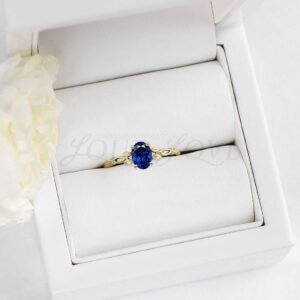 Oval sapphire solitaire ring with floral leaf motif displayed in a soft jewelry holder.