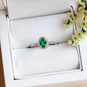 Thin silver band solitaire ring with oval lab emerald and a halo of side stones.