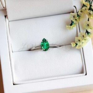 Emerald solitaire in pear-shaped setting displayed in a soft ring holder.