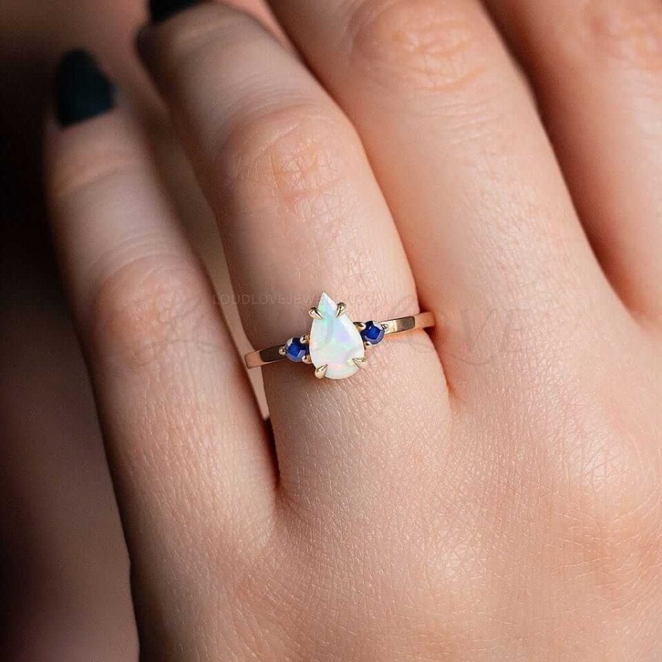 Natural pear opal flanked by deep blue sapphires, styled in a balanced and elegant three-stone look.