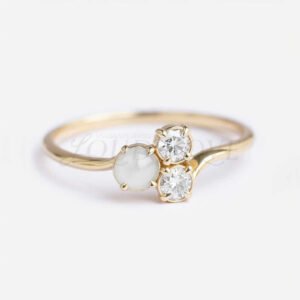 Asymmetrical cluster ring with round akoya pearl and two moissanites on a gold band.