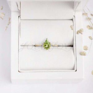 Soft yellow gold band with pear peridot center and white round stones, nestled in a refined display box.