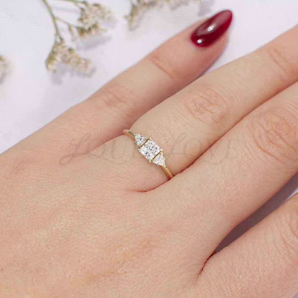 Yellow gold three-stone moissanite ring with princess cut and triangle side stones, worn on hand.