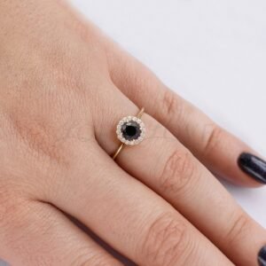 Rose gold engagement ring with round black diamond and white stone halo worn on hand.