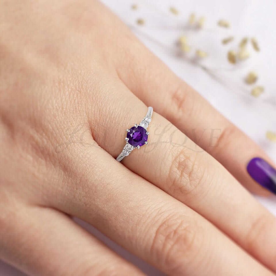 Classic white gold ring with central round amethyst and moissanite sides, styled on the hand.