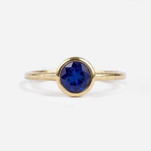 Round lab-grown sapphire bezel-set in a yellow gold solitaire engagement ring.