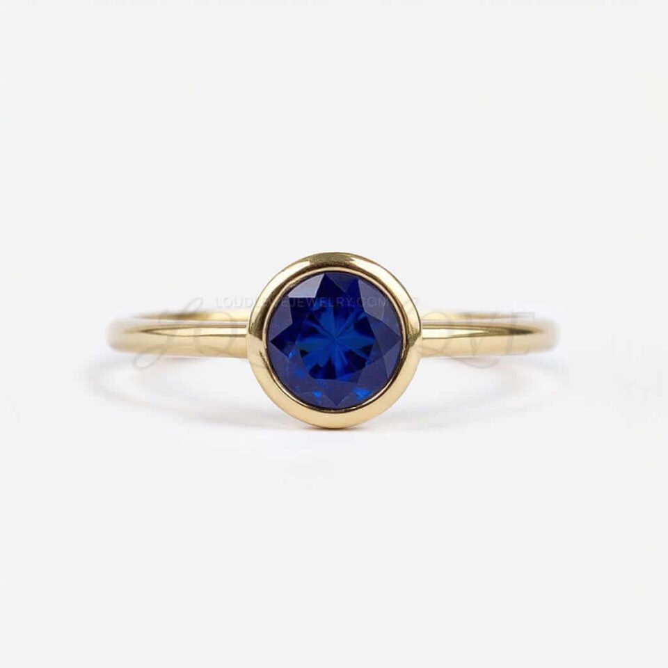 Round lab-grown sapphire bezel-set in a yellow gold solitaire engagement ring.