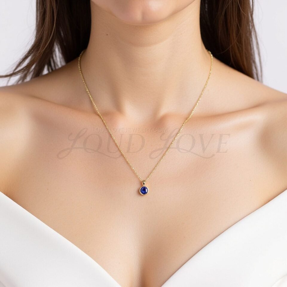 Deep blue sapphire pendant framed in gold, shown resting naturally at the neckline.