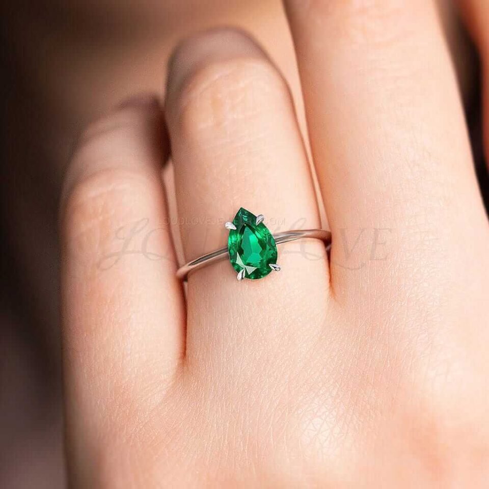Simple pear emerald solitaire in white gold worn as a modern engagement ring.