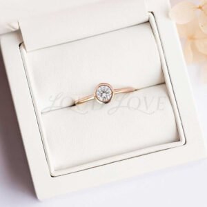 Bezel-set round moissanite solitaire ring with rose gold band for engagement.
