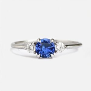 Round lab sapphire with one white side stone on each side in a classic three-stone design.