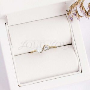 Gold engagement ring with pearl and lab diamond displayed in a soft cushioned case.
