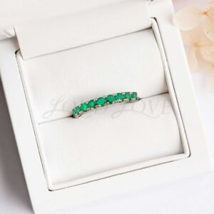 Nine-stone half eternity ring with lab emeralds displayed in a cushioned ring holder.